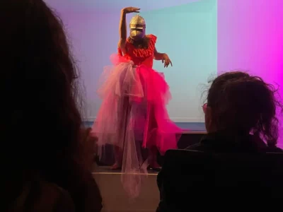 Sur un scène de théâtre, une femme habillée en robe de mariée avec un casque médiéval sur la tête