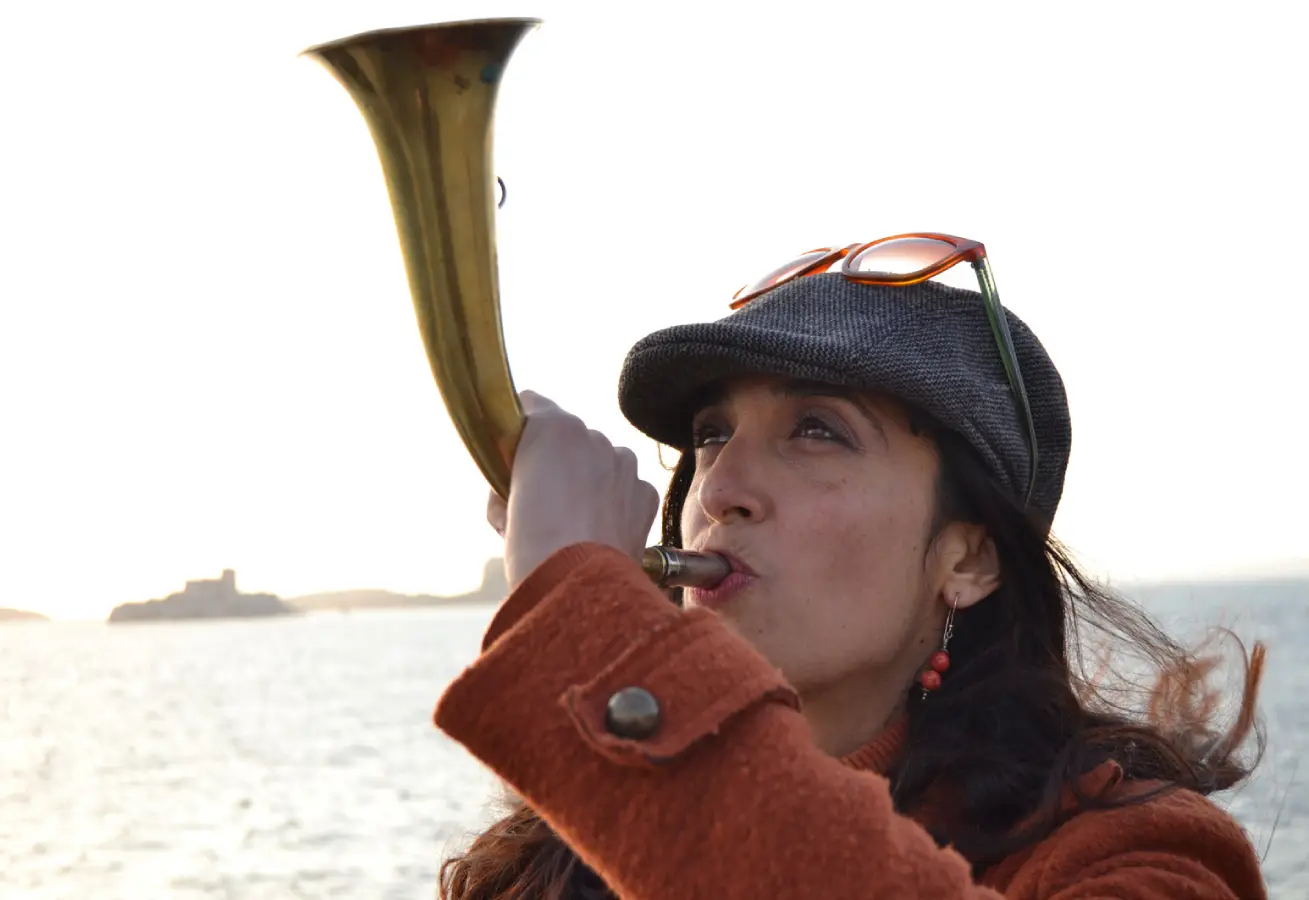 Une femme en train de jouer une corne, derrière elle, la mer
