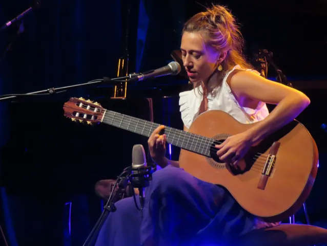 Photo en couleur d'une jeune femme devant un micro, en train de jouer la guitare