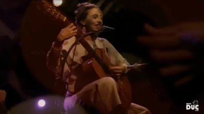 Une jeune femme souriante sur une scène musicale, en train de jouer la guitare et de chanter