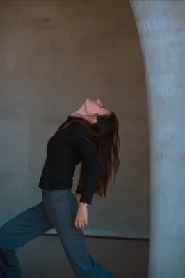 Une jeune femme aux cheveux longs esquisse un mouvement dansé de profil
